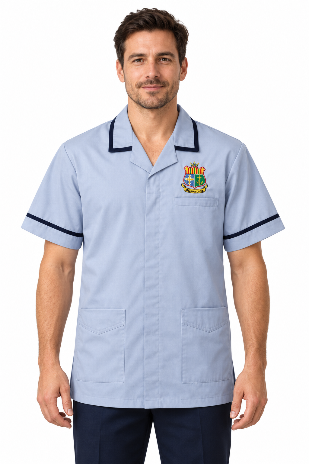 A man wearing a light blue short-sleeve scrub top with dark navy piping on the collar and sleeve cuffs, featuring a colorful medical crest on the left chest, set against a plain white background.